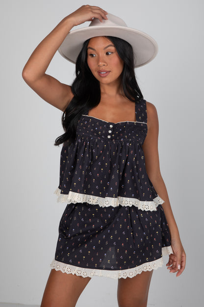 Woman wearing a black patterned dress with white lace trim and a white hat on a gray background
