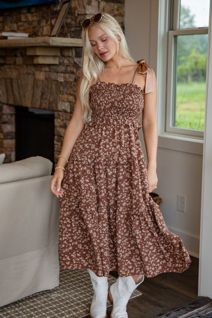 Woman in a floral dress standing in a room with a stone fireplace and window.
