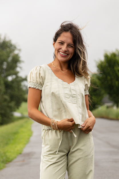 Woman in a light green outfit standing on a road with trees in the background
