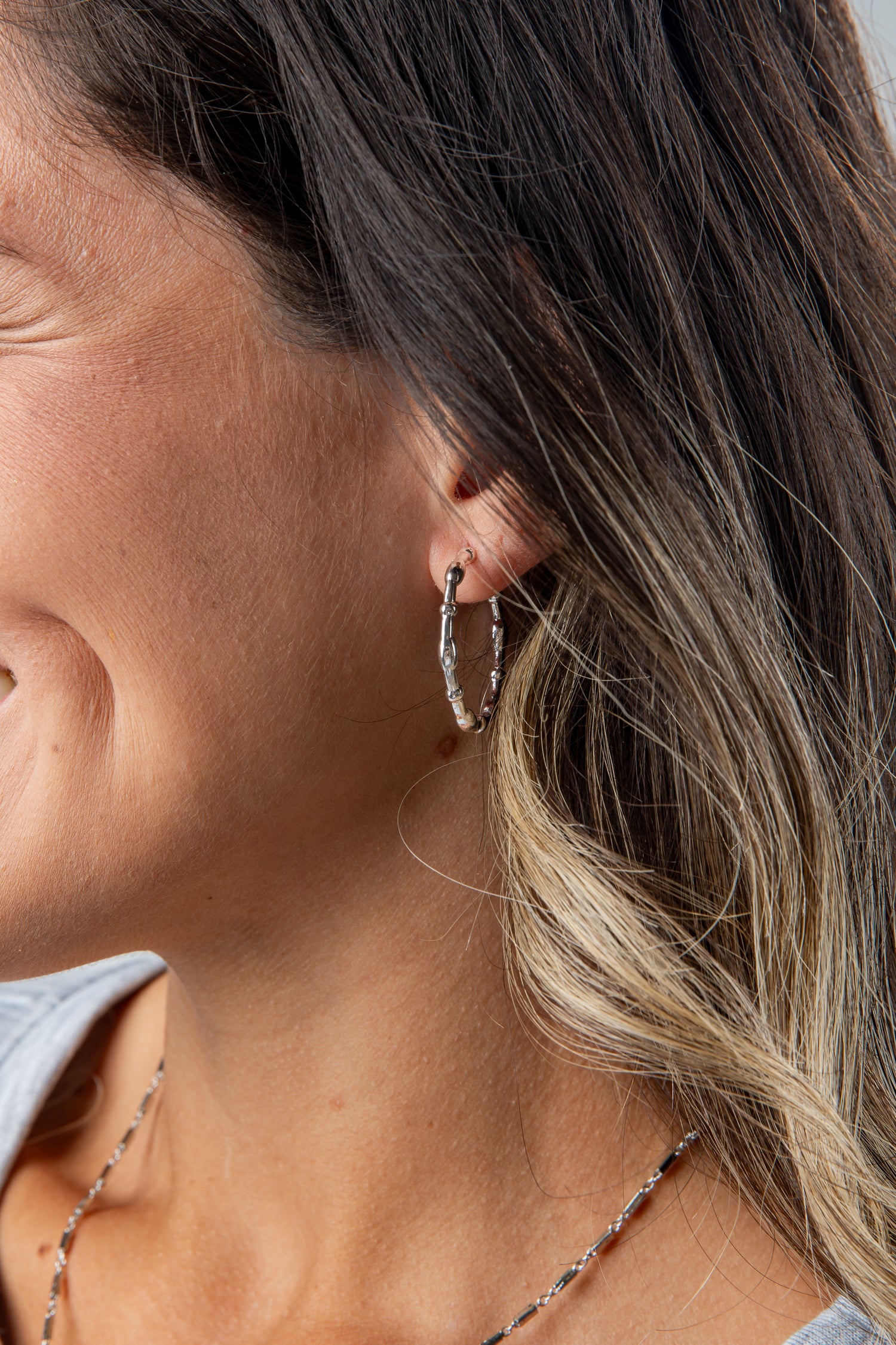 Close-up of a woman wearing silver hoop earrings with a neutral background