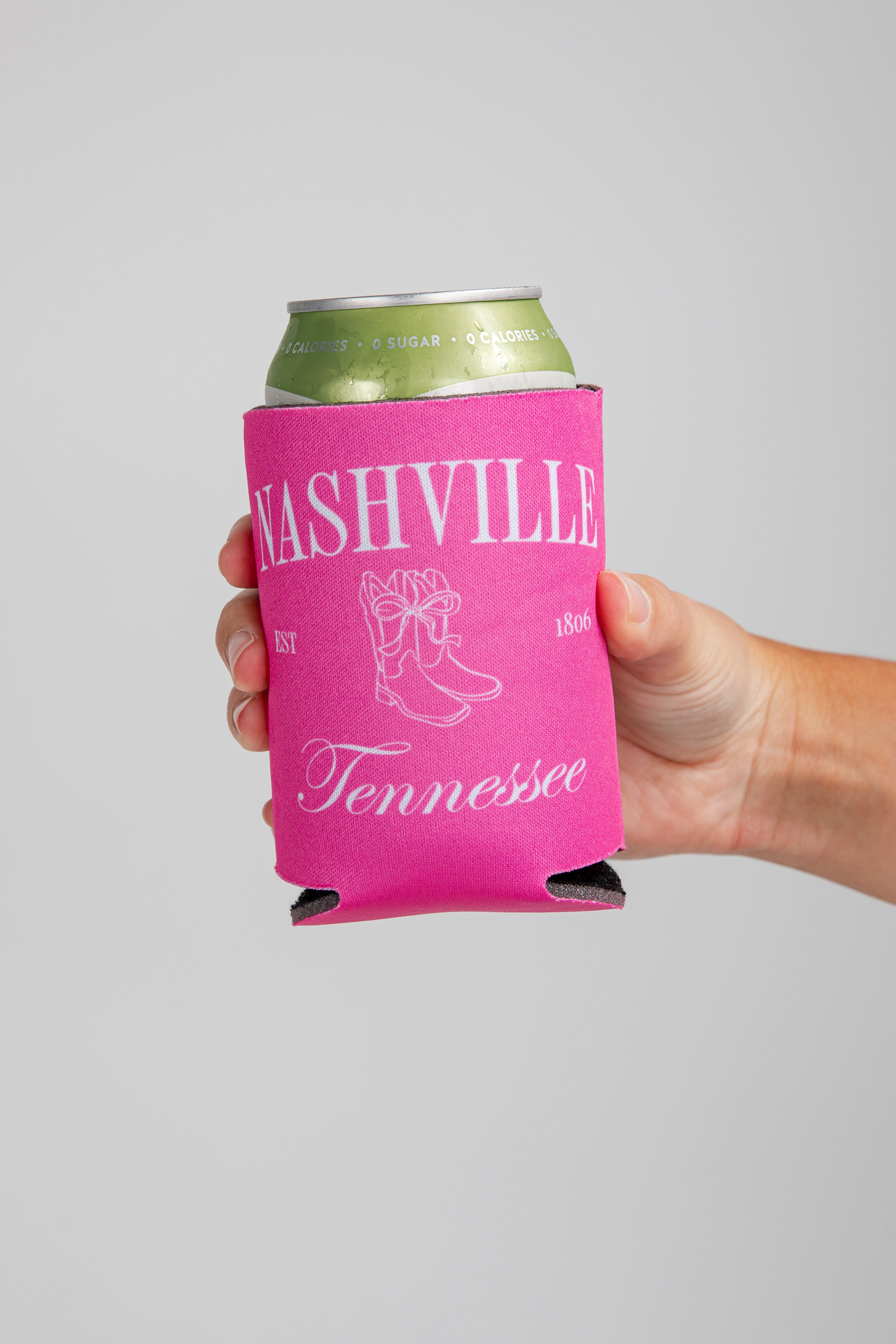 Hand holding a can with a pink Nashville, Tennessee koozie on a gray background