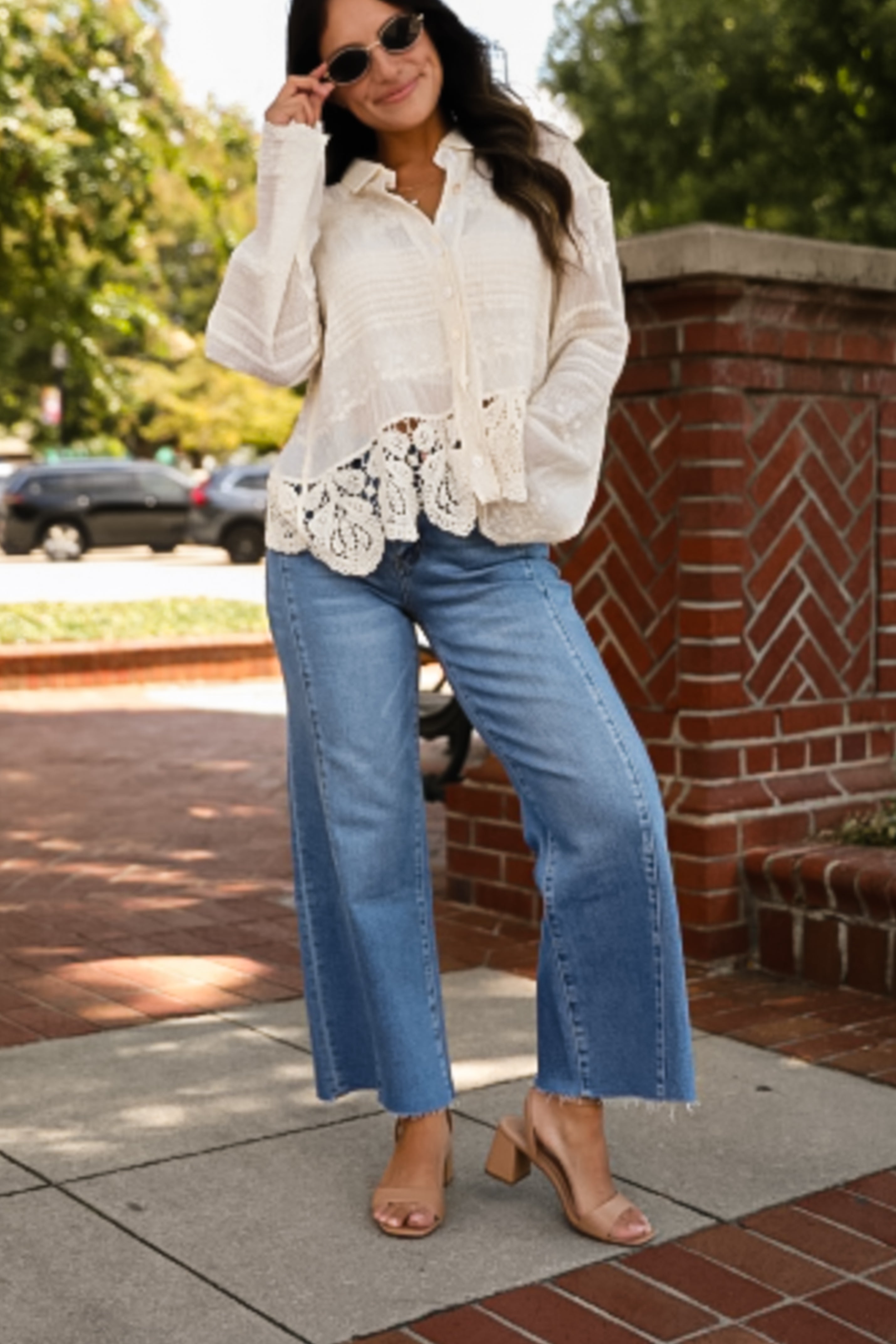 Woman wearing a white blouse with lace details and blue jeans standing outdoors.