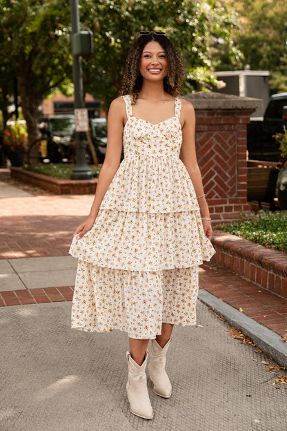 Woman in a floral dress standing on a sidewalk with trees and buildings in the background