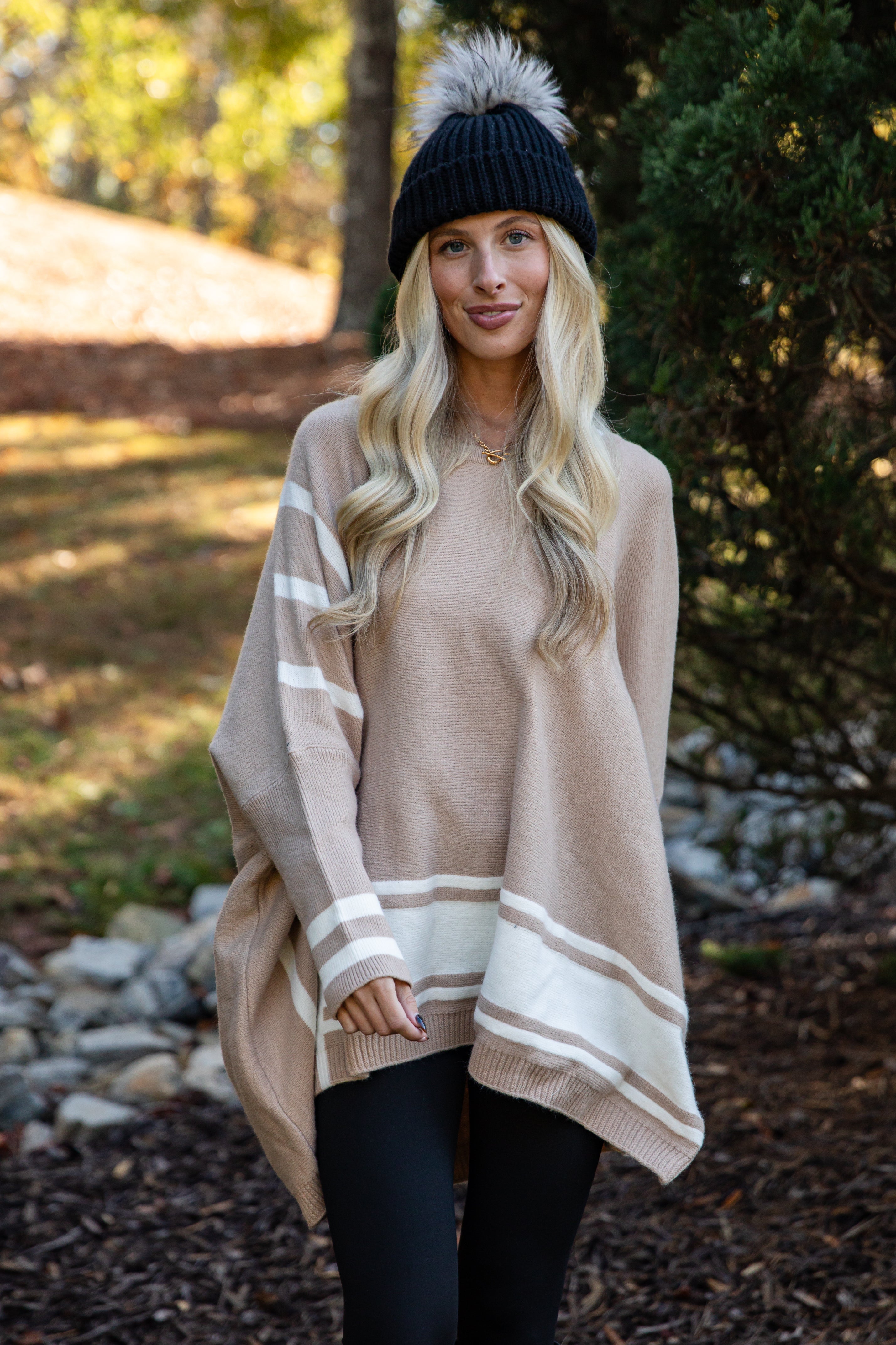 Woman wearing a beige poncho with white stripes outdoors in a natural setting