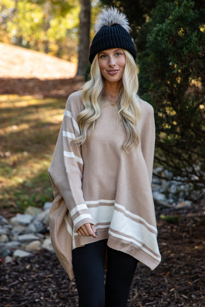 Woman wearing a beige poncho with white stripes outdoors in a natural setting