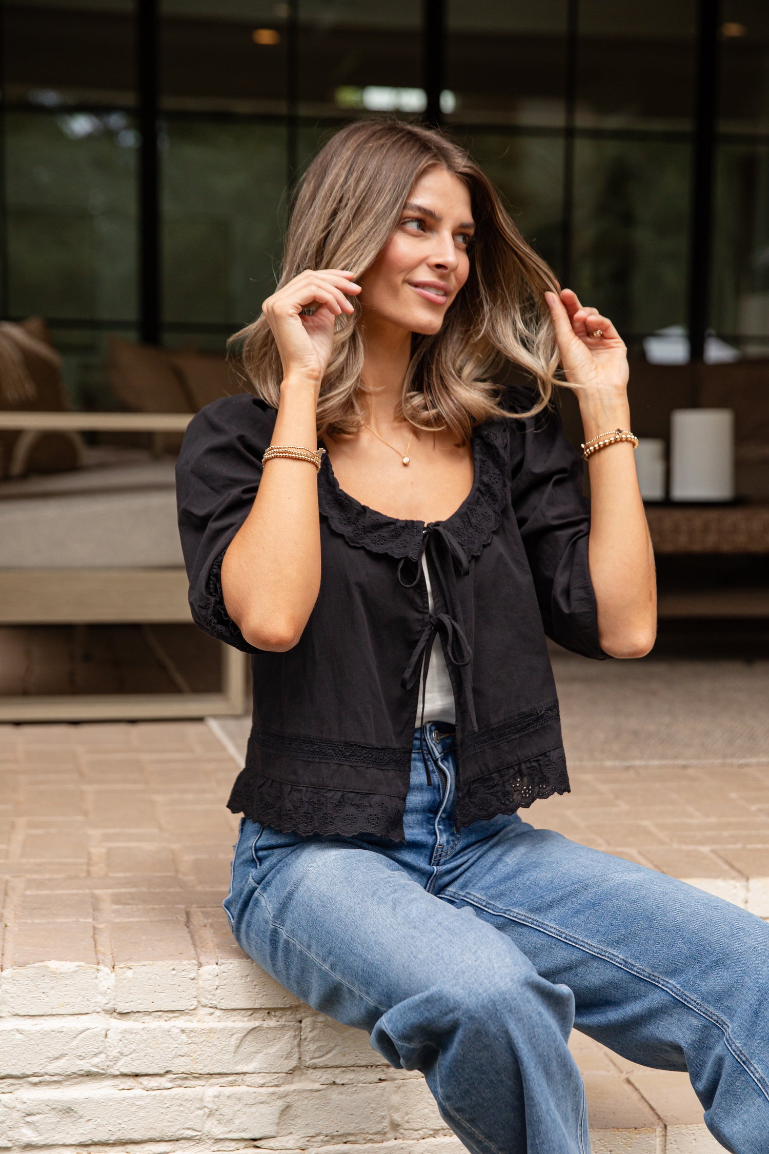 Woman wearing a black top and blue jeans sitting outdoors.