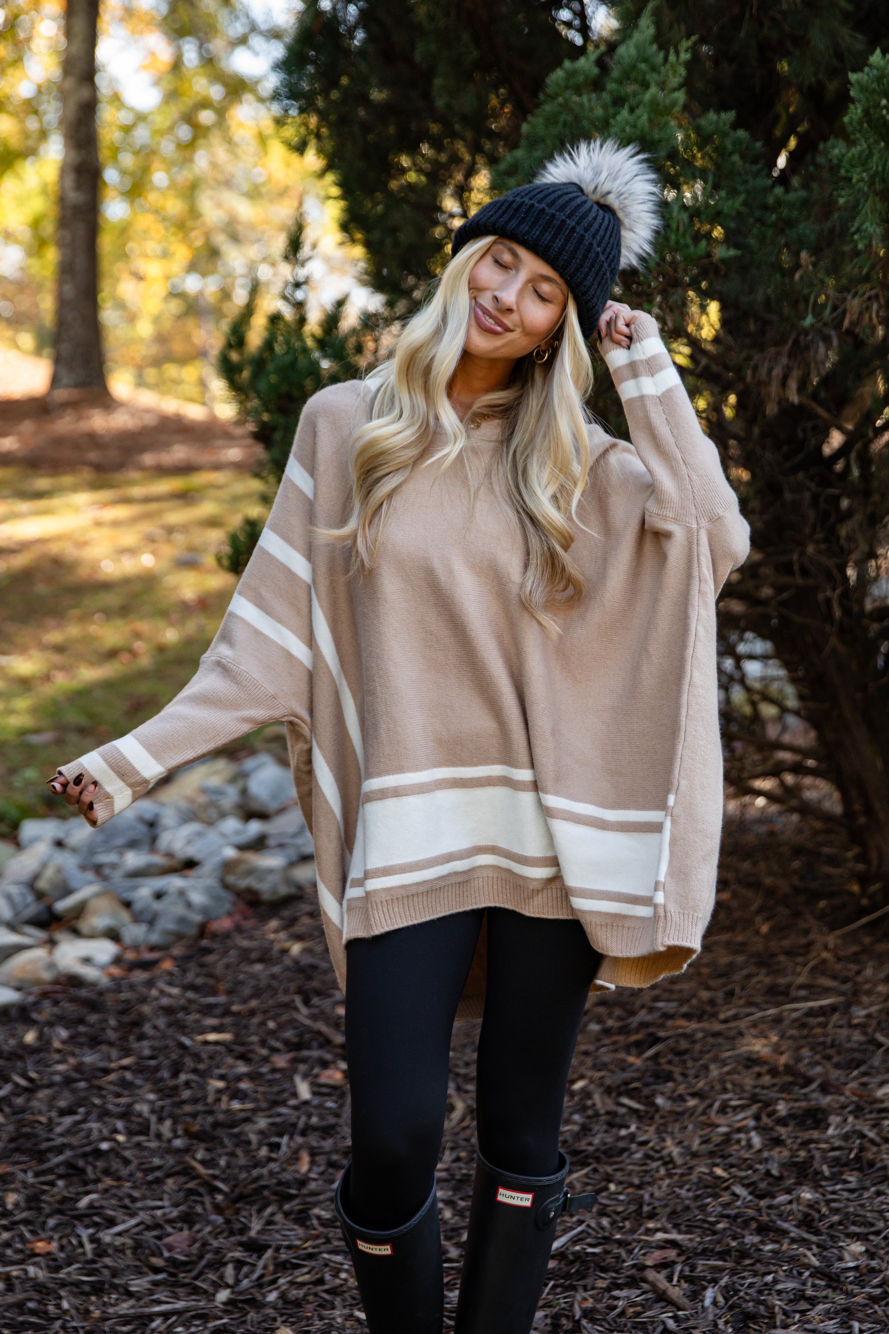 Woman wearing a beige and white striped poncho in a forest setting