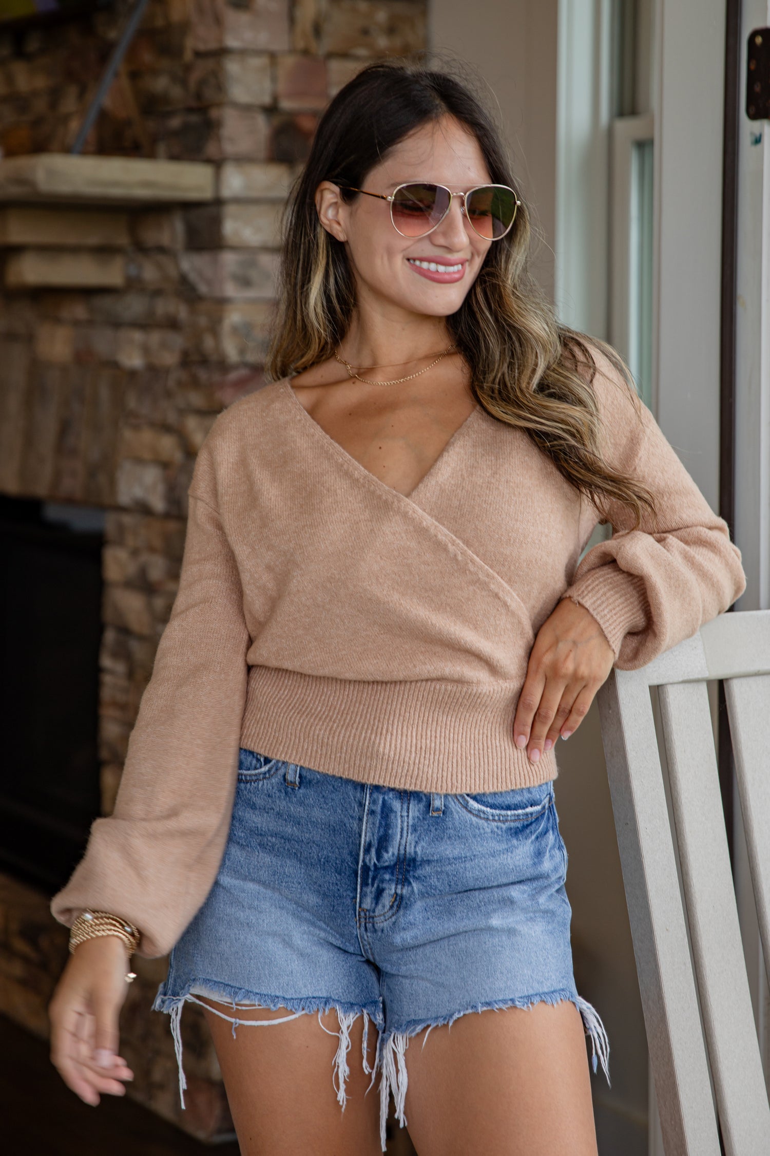 Woman wearing a beige sweater and denim shorts standing indoors.