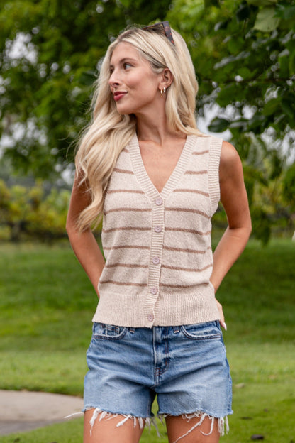 Woman wearing a beige sleeveless top, denim shorts, and beige knee-high boots standing on grass.