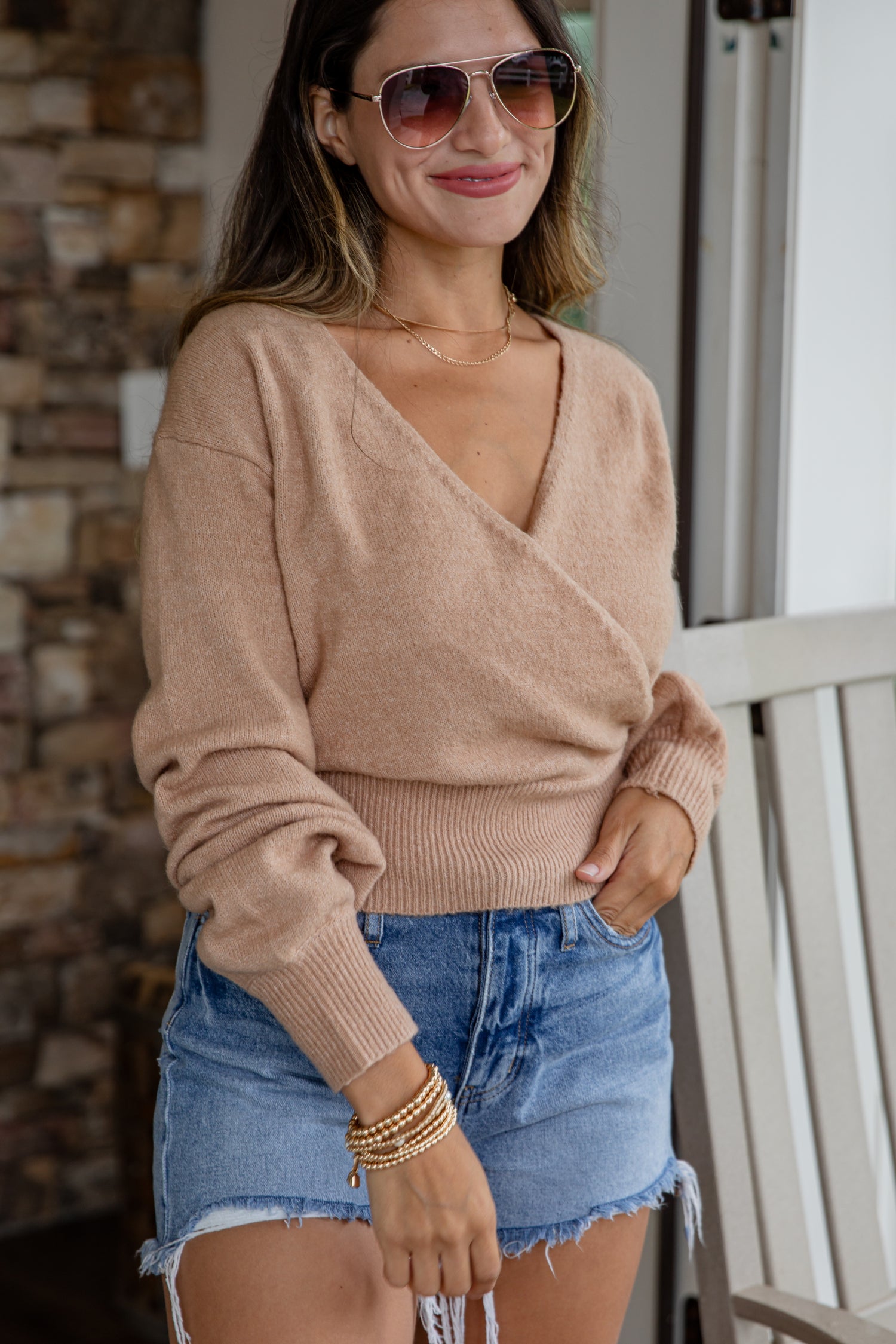 Woman wearing a beige sweater and denim shorts outdoors.