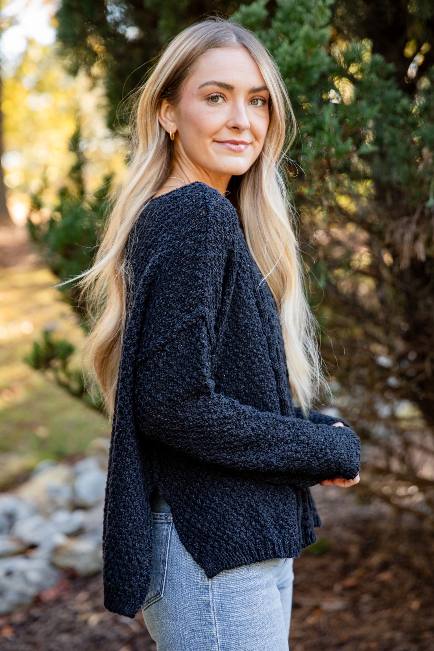 Woman wearing a dark blue sweater standing outdoors with trees in the background