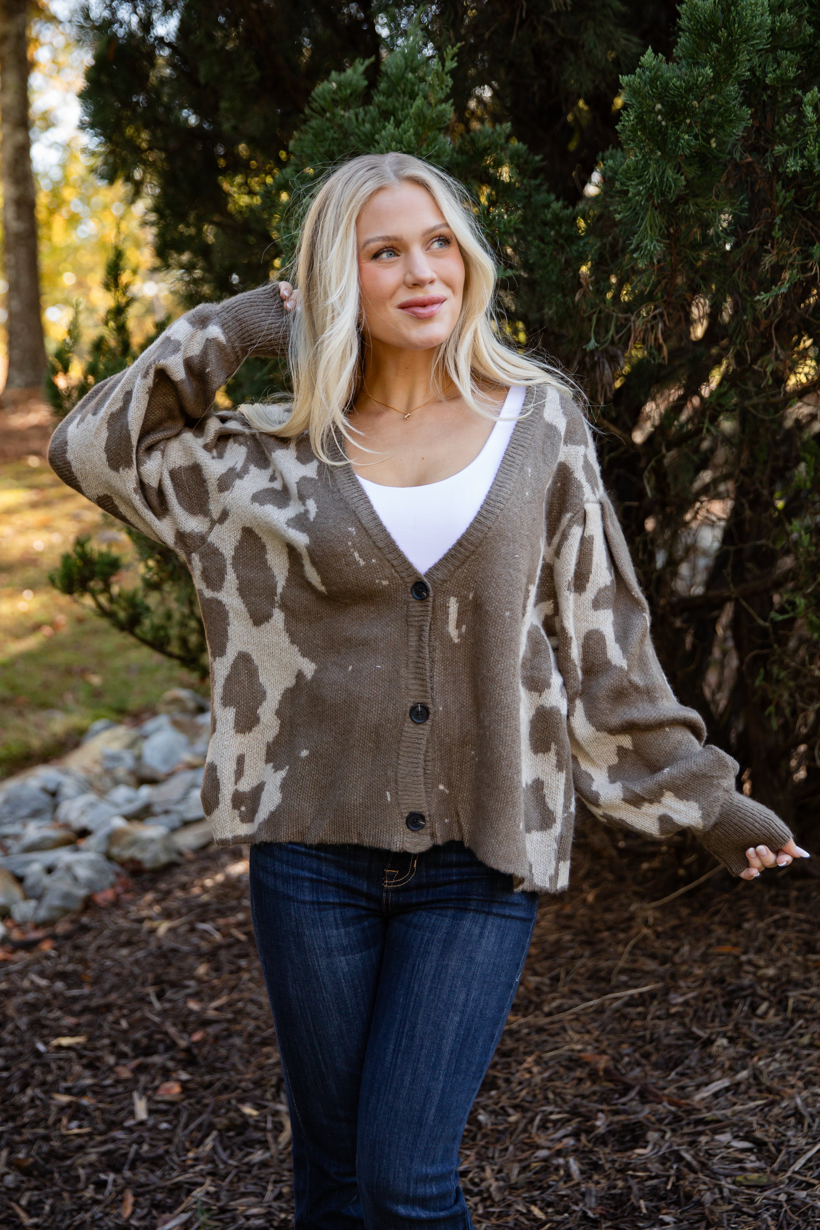 Woman wearing a patterned cardigan outdoors with trees in the background