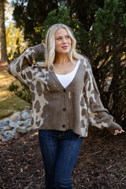 Woman wearing a patterned cardigan outdoors with trees in the background