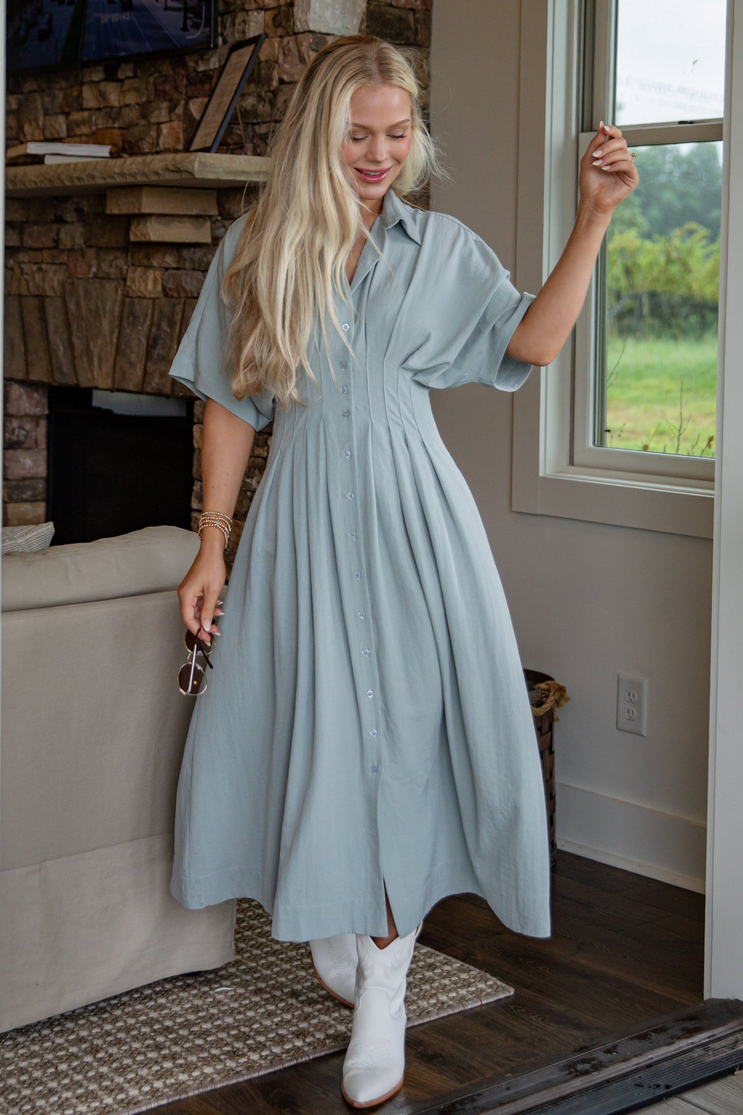 Woman in a light blue dress standing in a room with a fireplace and window.