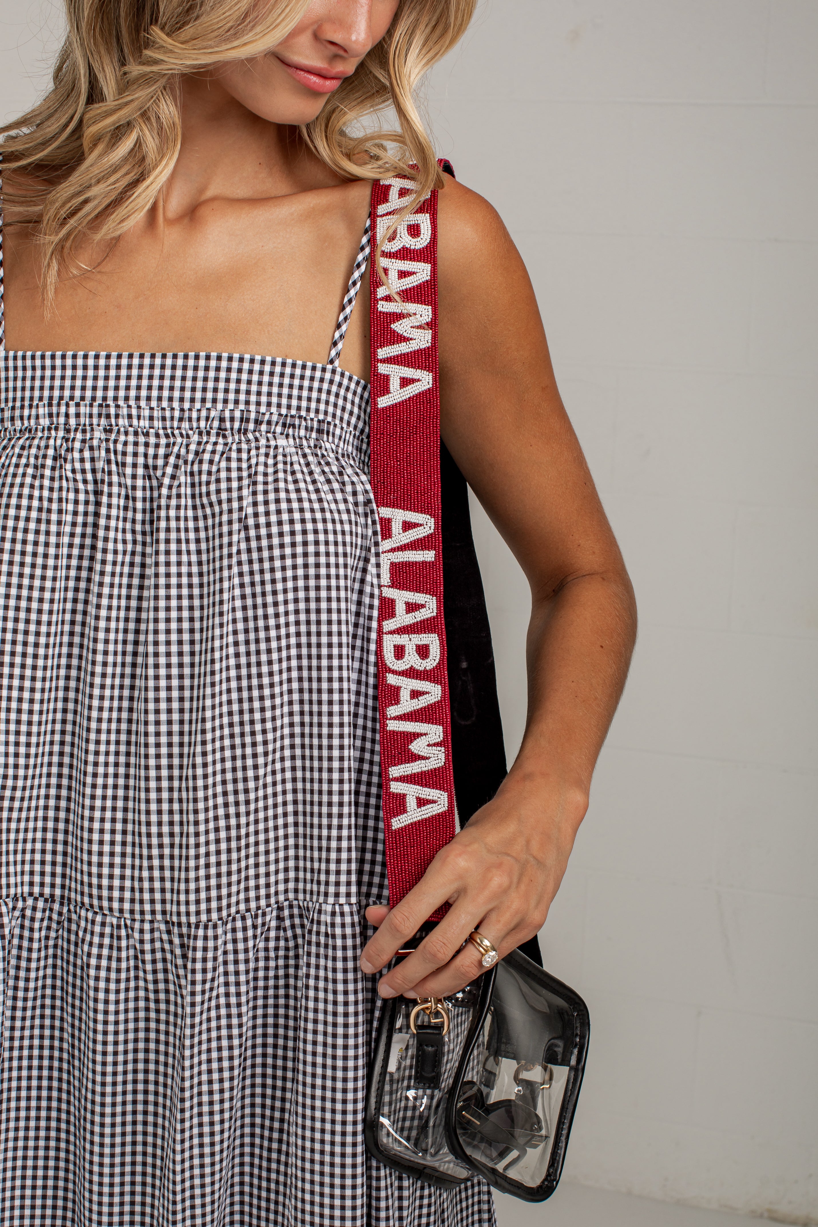 A woman wearing a black and white gingham dress carries a small black handbag with a wide red shoulder strap printed with &