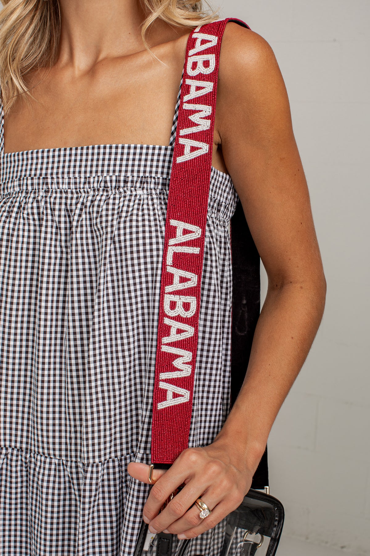 Close-up of a woman wearing a black and white gingham dress and holding a red shoulder strap with &