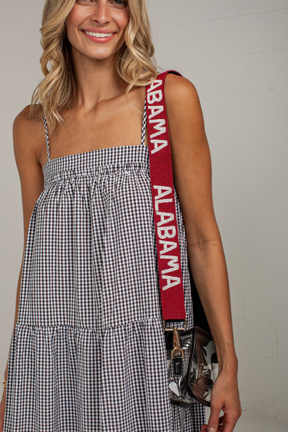 A woman wearing a black and white gingham tiered dress with a crimson red shoulder strap featuring the words &