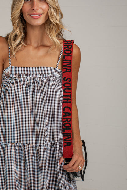 A woman wearing a black and white gingham dress holds a red shoulder strap with &