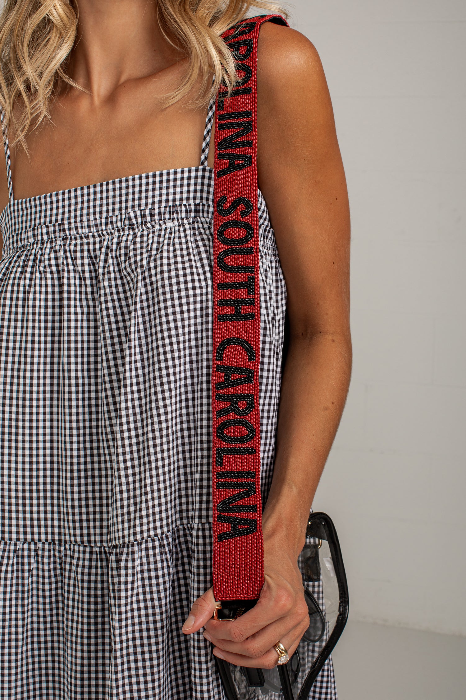 A close-up of a person wearing a black and white gingham dress, holding a red shoulder strap with &