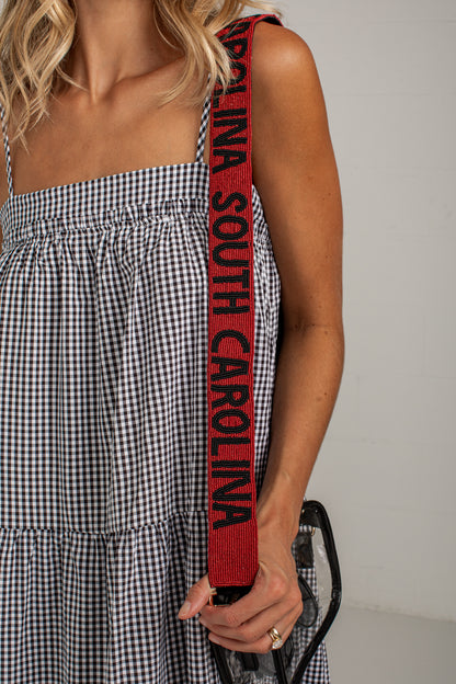 A close-up of a person wearing a black and white gingham dress, holding a red shoulder strap with &