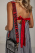 A woman shown from the back wearing a black and white gingham dress with a red back bow and a red shoulder strap printed with &