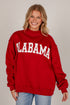 A smiling blonde woman wearing a red mock-neck sweatshirt with &