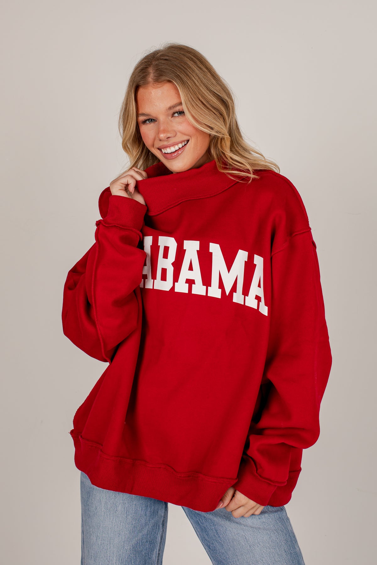 A smiling blonde woman wearing an oversized red sweatshirt with &