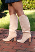 Beige knee-high boots on a person standing on a brick path with grass in the background