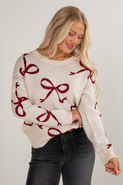 Woman wearing a cream sweater with red bow patterns on a plain background