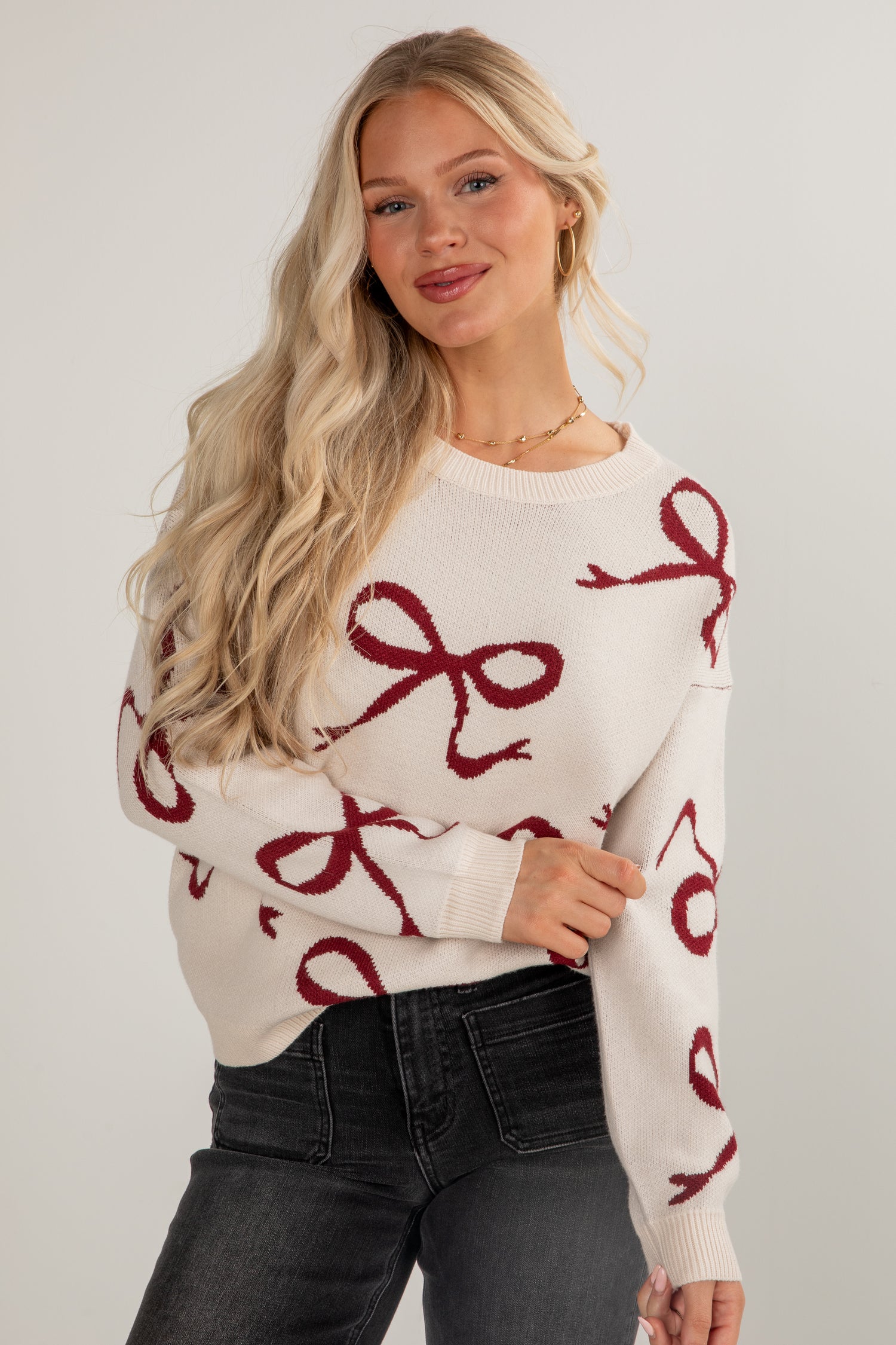 Woman wearing a white sweater with red bow patterns on a plain background
