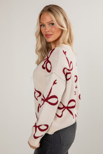 Woman wearing a cream sweater with red patterns on a plain background