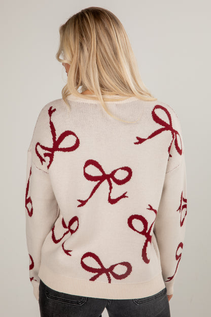 Woman wearing a cream sweater with red bow patterns on a plain background