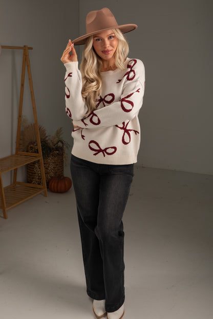 Woman wearing a sweater with red patterns and a hat, standing in a minimalistic room.