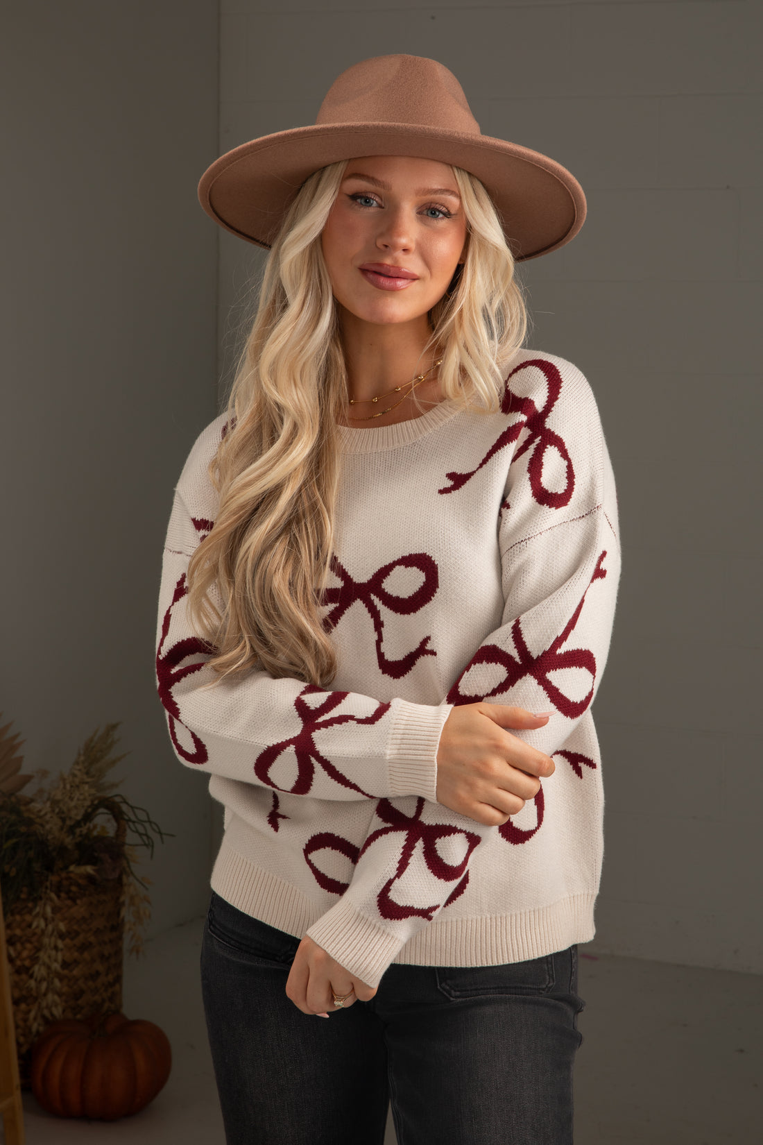 Woman wearing a white sweater with red patterns and a brown hat indoors.