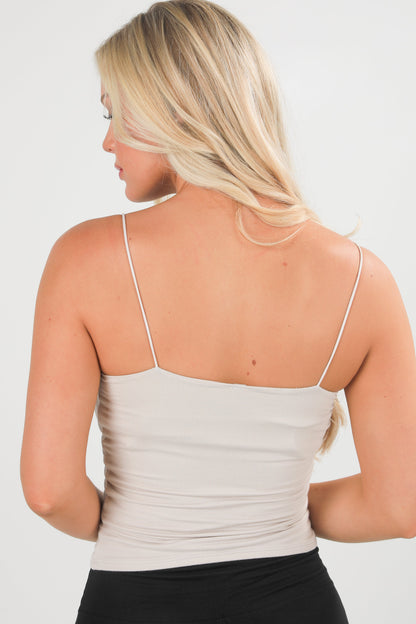 Woman wearing a beige tank top with thin straps on a plain background