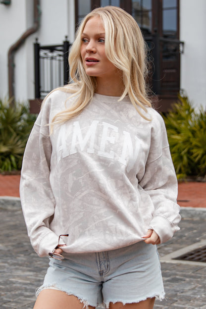 Woman wearing a light gray sweatshirt with text and denim shorts outdoors.