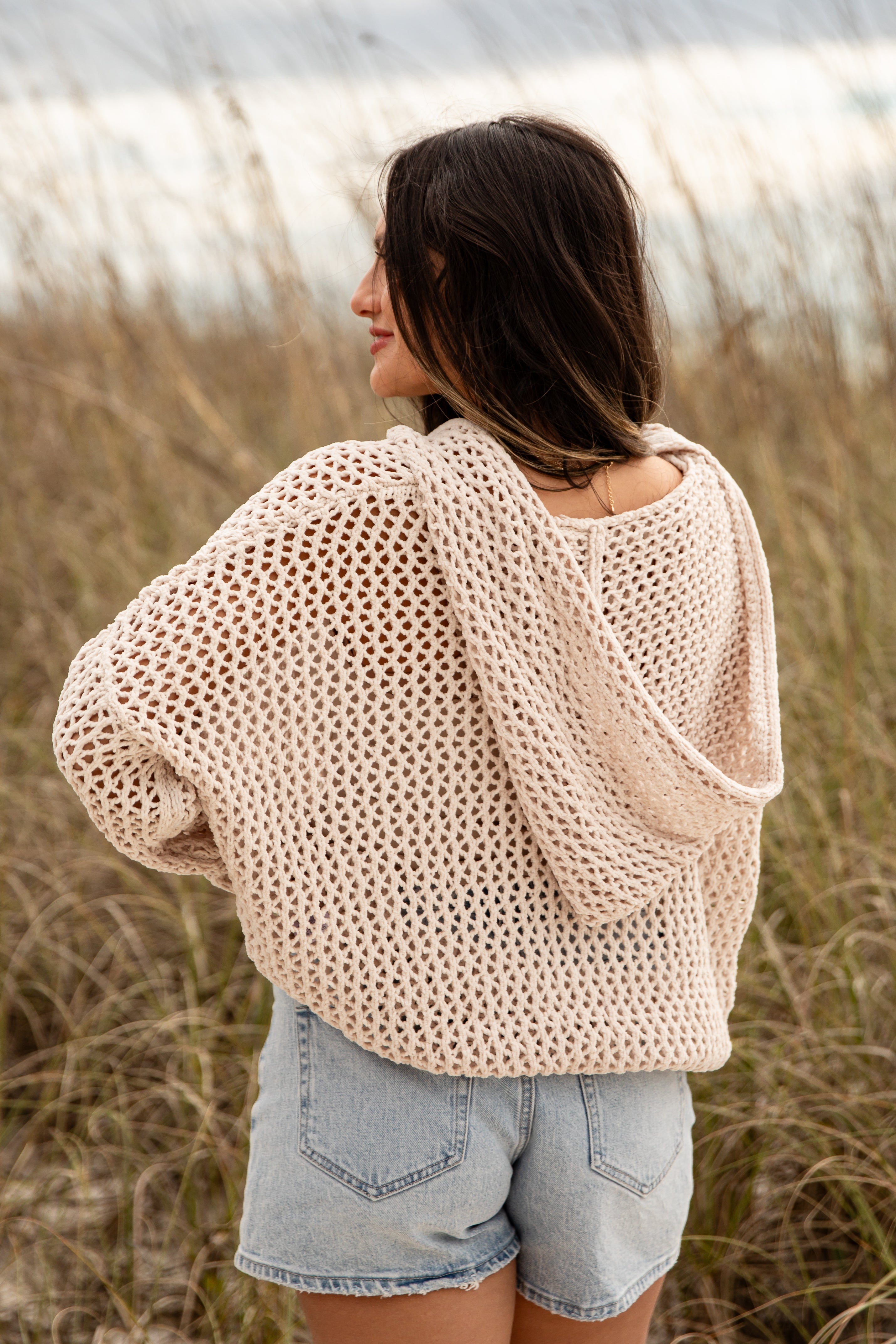 Woman wearing a beige oversized sweater and denim shorts standing in a field.