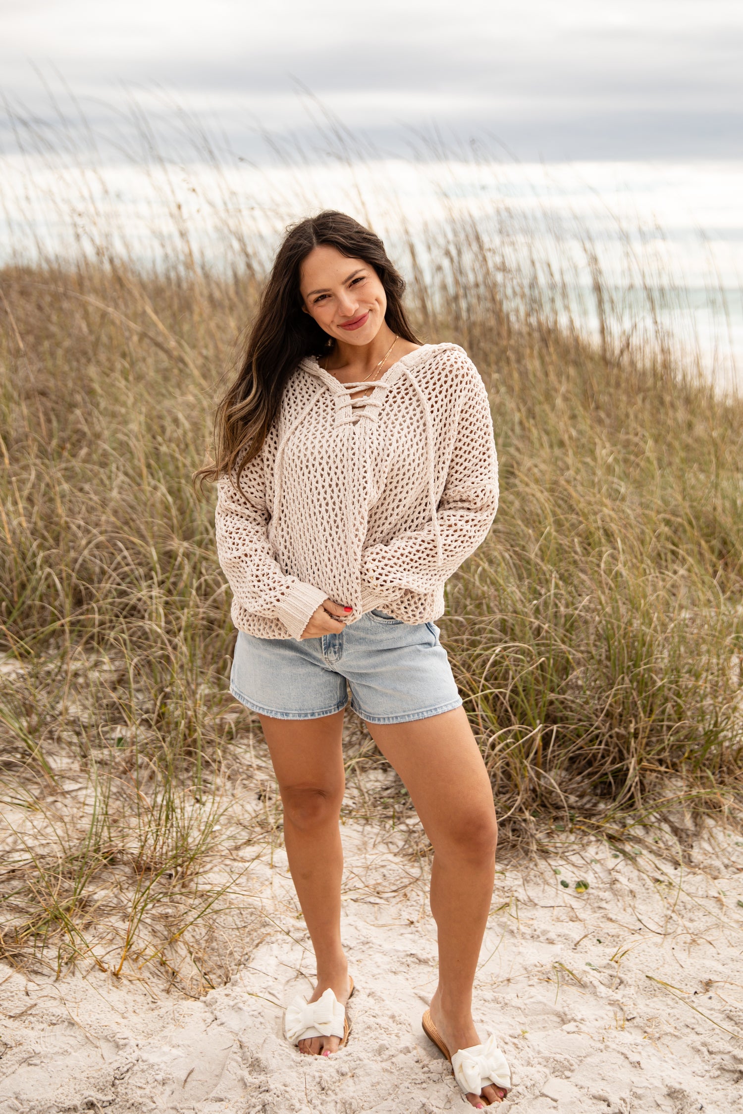 Woman standing on a sandy beach with grassy dunes and ocean in the background