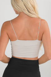 Woman wearing a beige tank top with thin straps on a plain background
