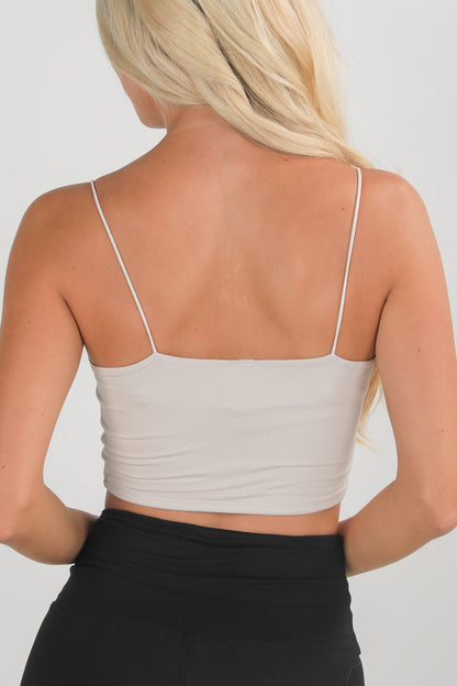 Woman wearing a beige tank top with thin straps on a plain background