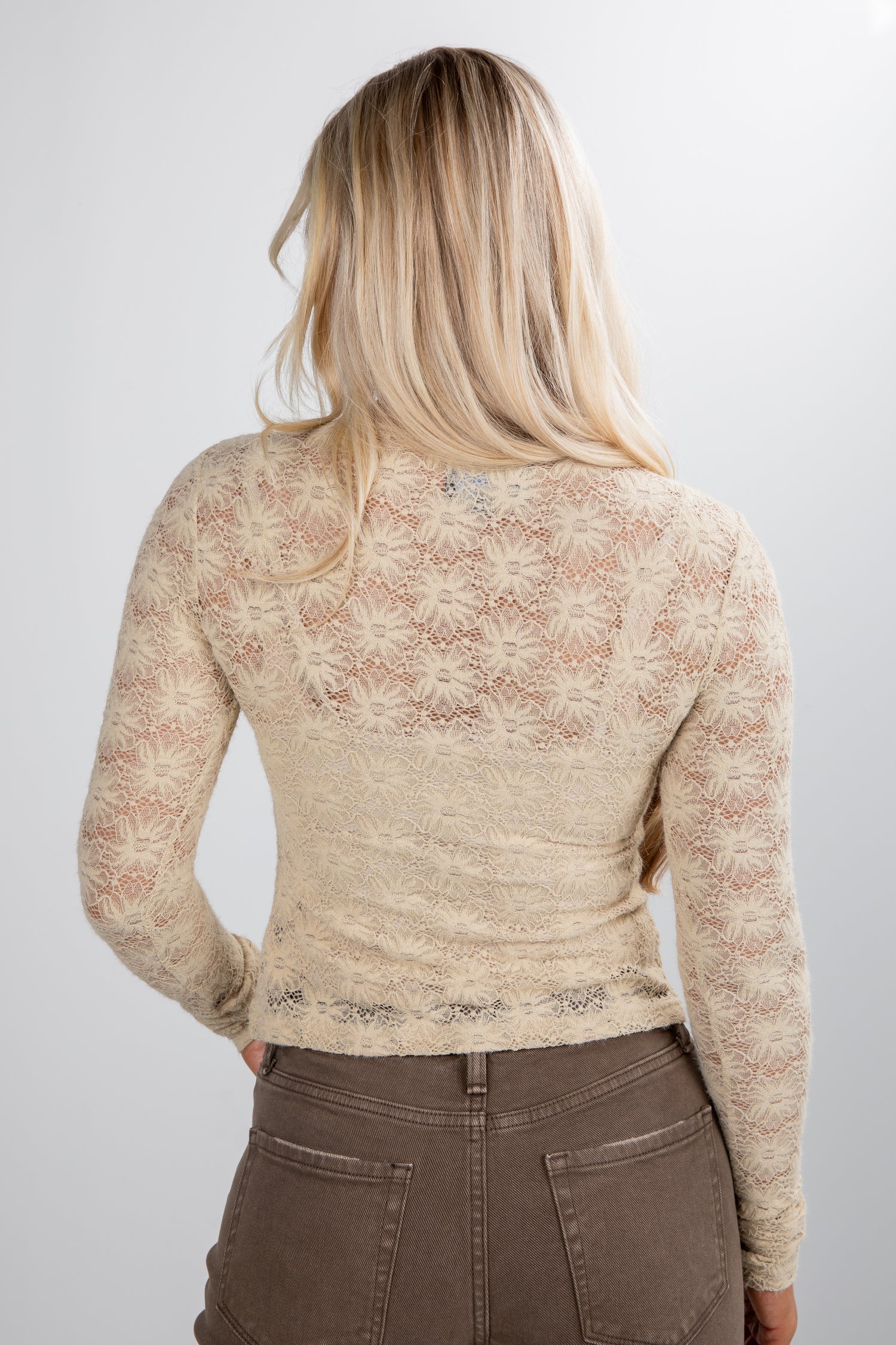 Person wearing a beige lace top and brown pants on a white background