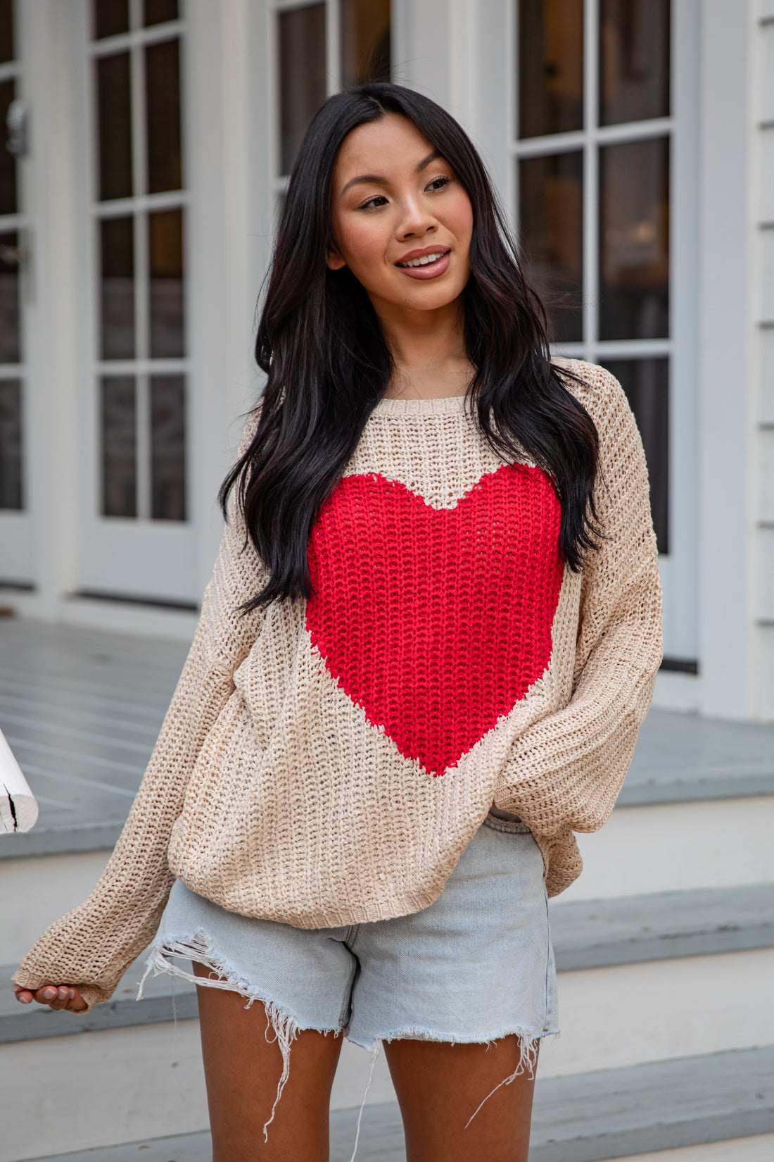 Woman wearing a beige sweater with a red heart design outdoors.