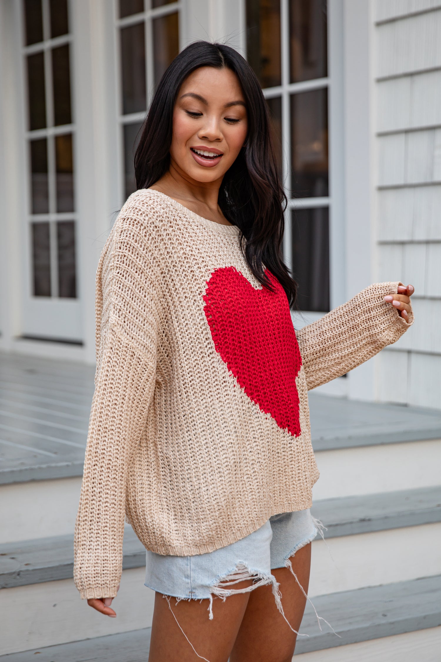 Woman wearing a beige sweater with a red heart design outdoors.