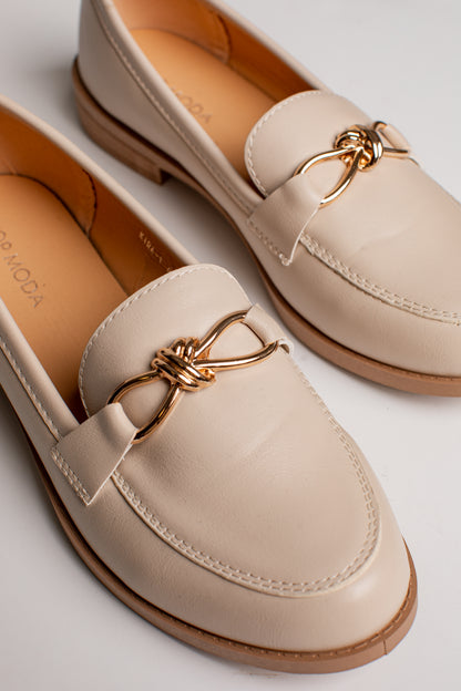 A pair of beige leather penny loafers with a decorative gold-tone metal bow detail across the vamp, shown on a clean white background.