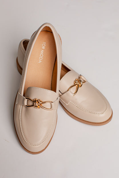 A pair of cream-colored leather loafers with gold-tone metal bow details, displayed on a light gray background. The brand name &