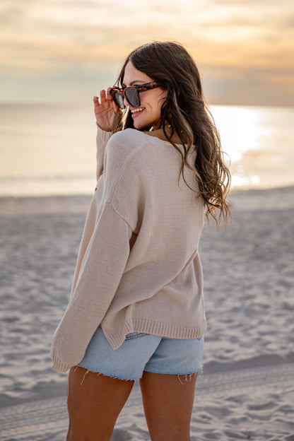 Woman on a beach at sunset wearing a beige sweater and denim shorts.