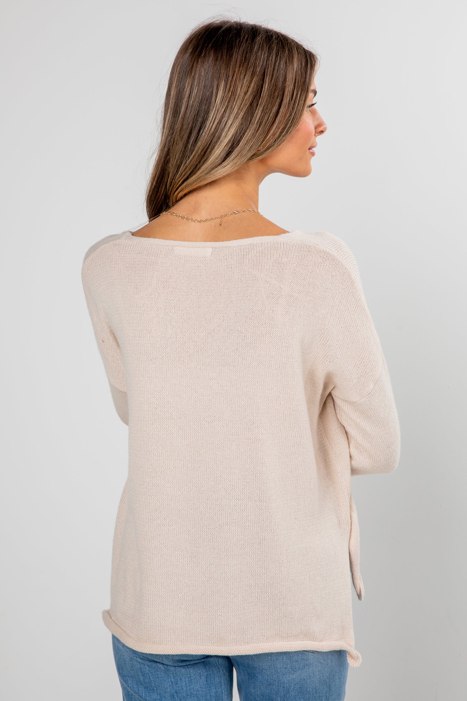 Woman wearing a beige sweater and blue jeans on a plain background