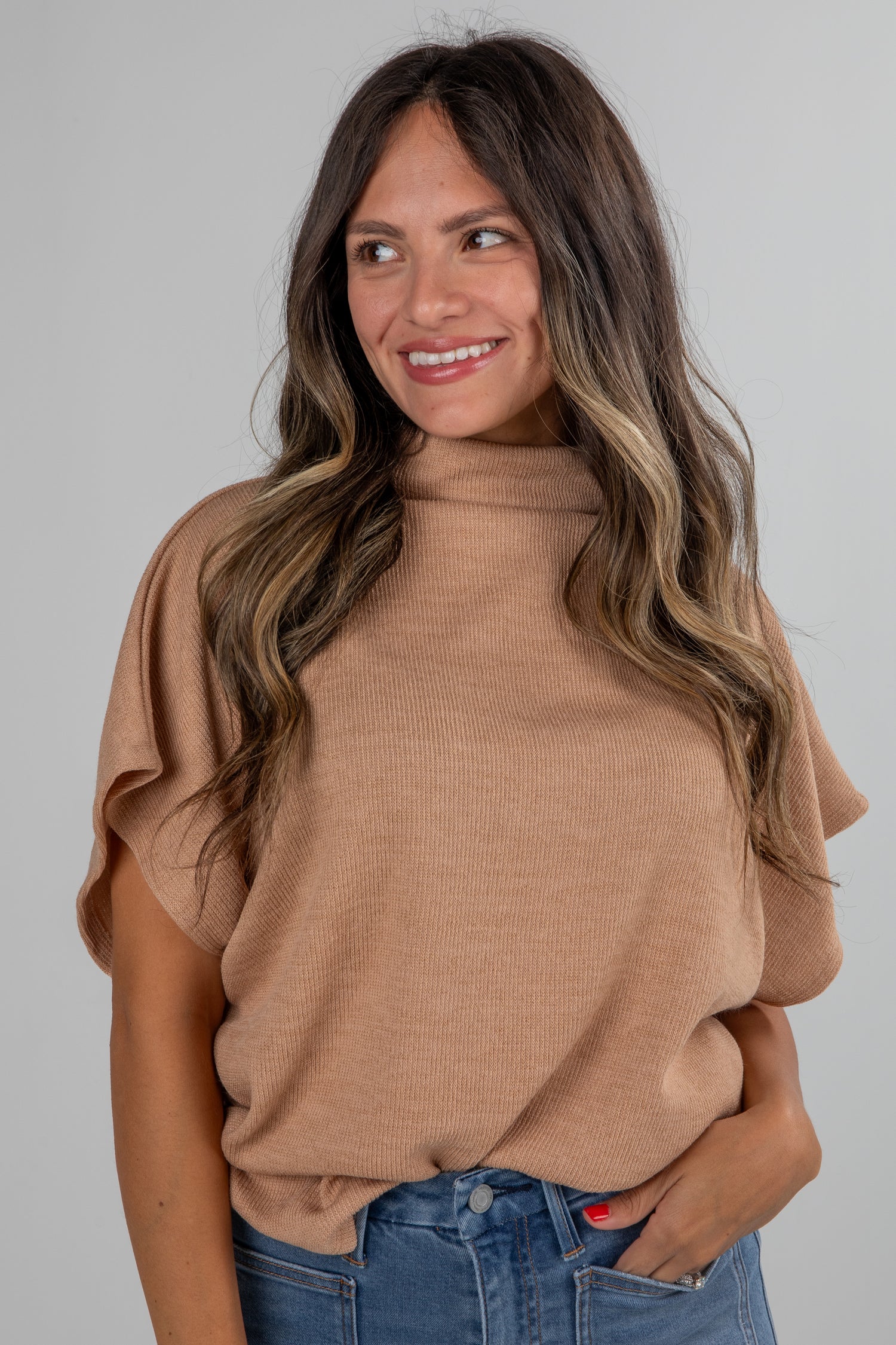 Woman wearing a brown sweater and blue jeans against a gray background