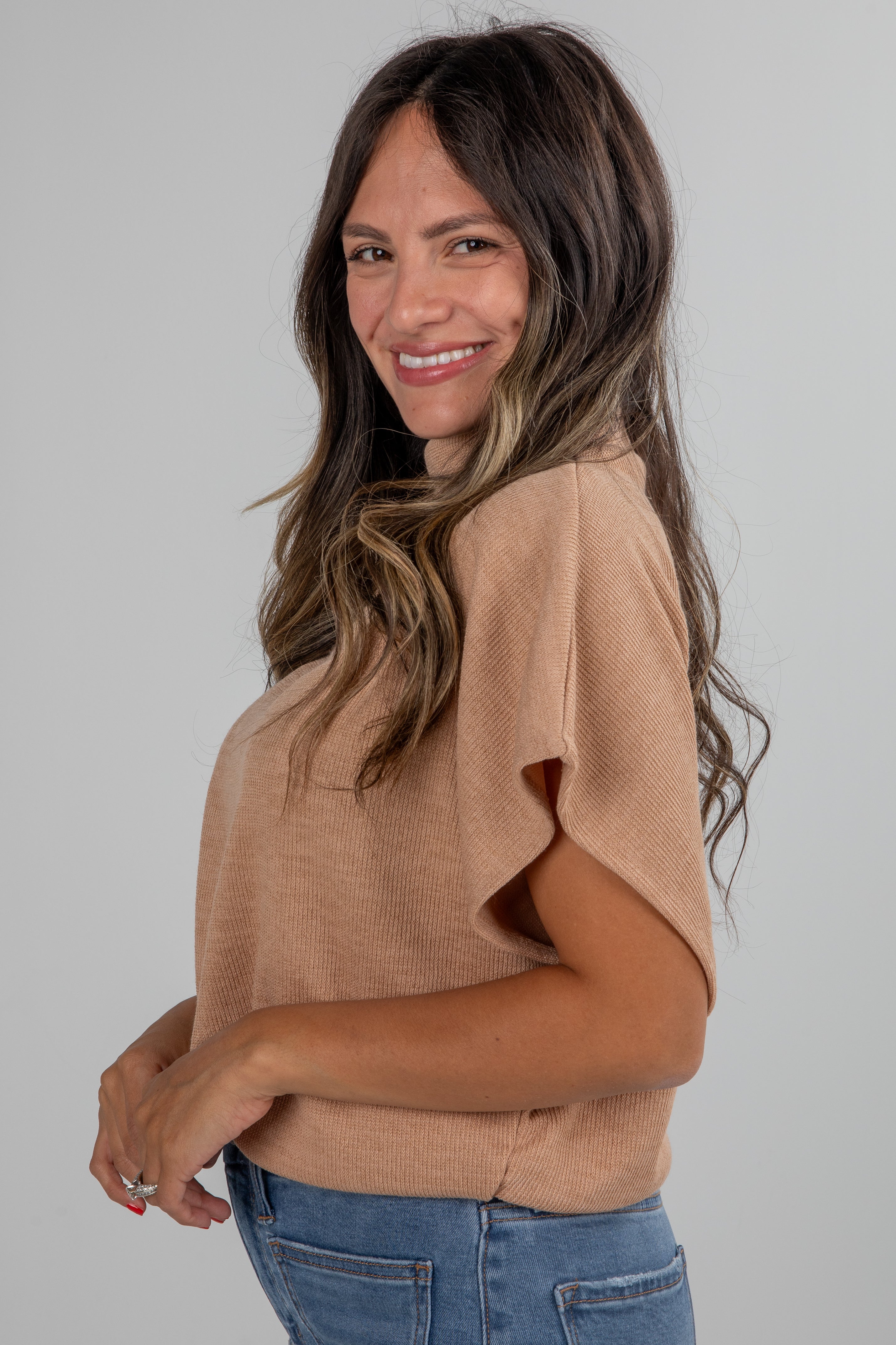 Woman wearing a beige top and blue jeans against a plain background