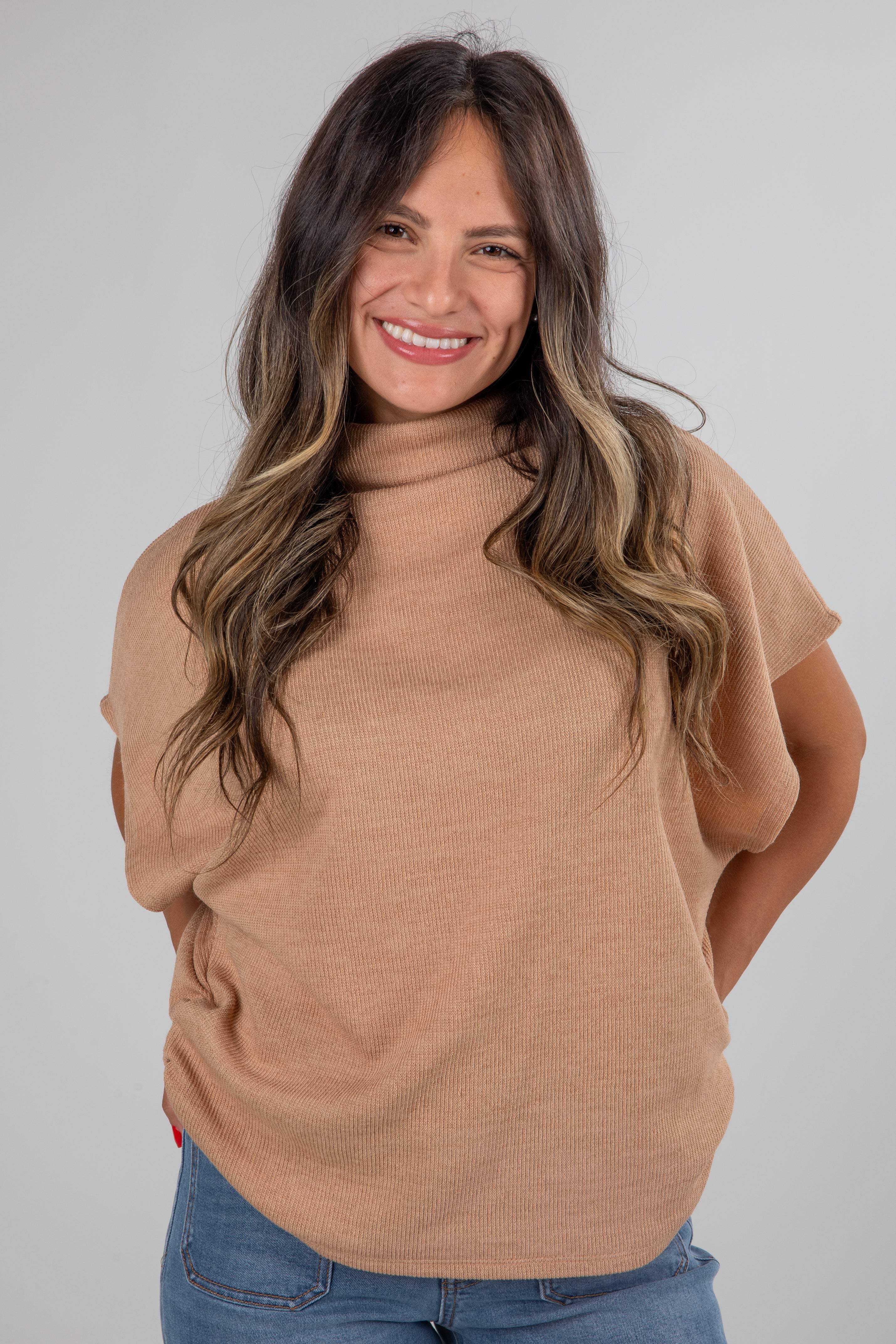 Woman wearing a beige sweater and blue jeans against a gray background